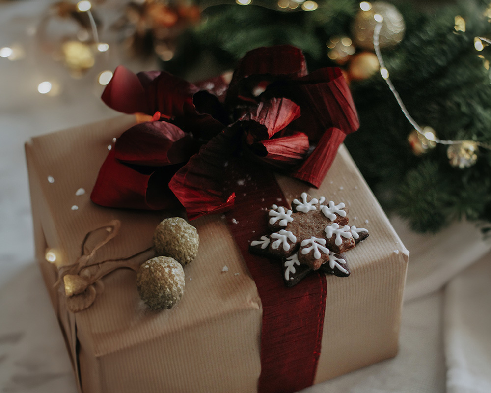 Karácsonyi ajándék papírba csomagolva, masnival átkötve és sütivel díszítve.