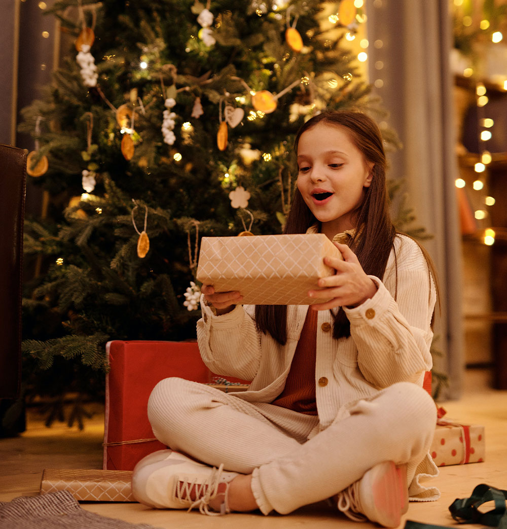 Egy lány örül az ajándéknak a karácsonyfa alatt.