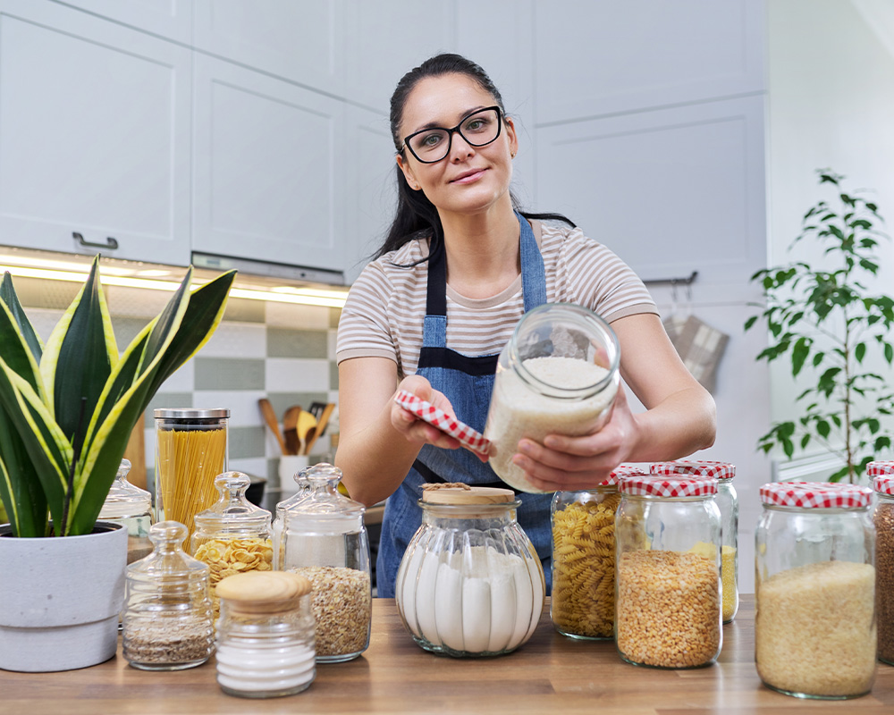 A nő a konyhában mutatja a száraz élelmiszerek tárolására szolgáló edényeket