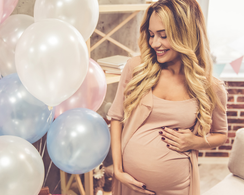 Terhes nő mosolyogva nézi a színes lufikat egy babavárón