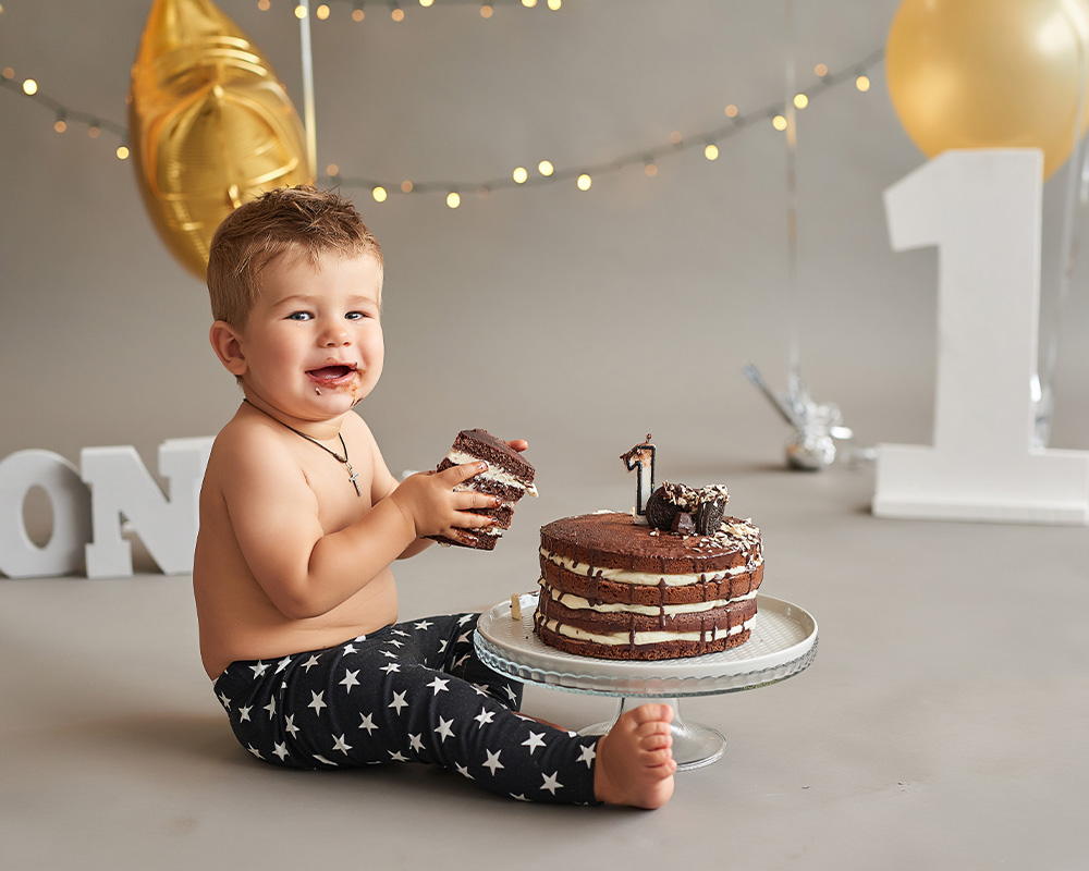 Egyéves kisfiú egy szelet csokoládétortát tart a kezében születésnapja alkalmából