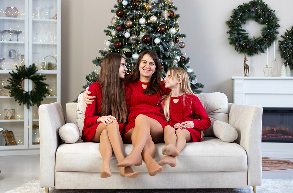 Az anya és lányai piros ruhákban együtt töltik az ünnepi időt a karácsonyfa mellett.